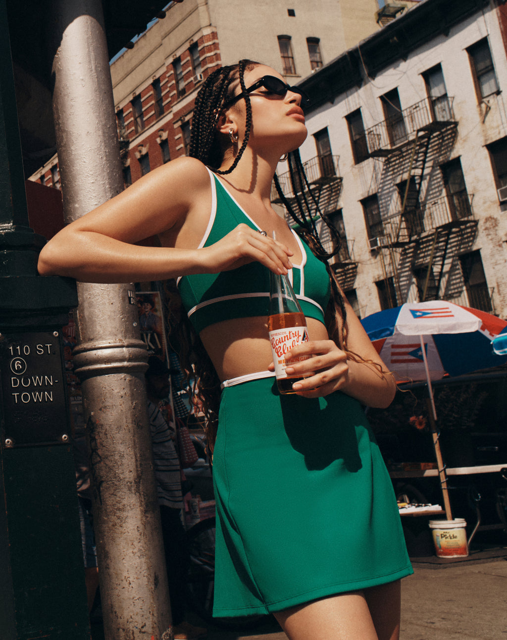 Model wearing a green sports bra and skirt from All Access drinking a soda while standing on the street in New York