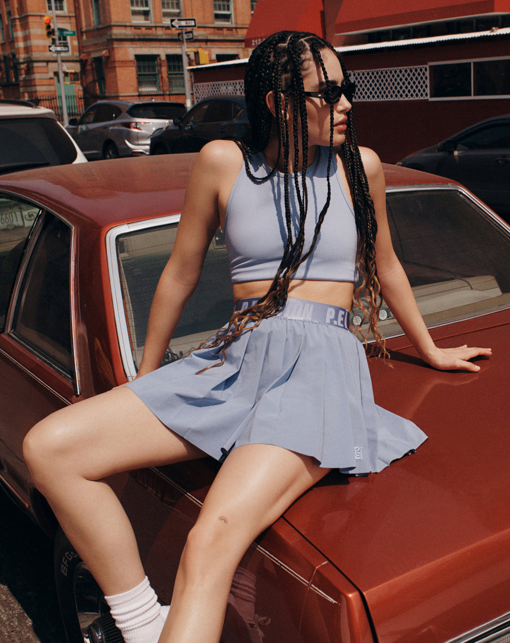 Model wearing a purple tank top and skirt from P.E Nation sitting on top of a red car outside in New York